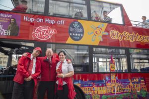 Two men and a woman who work for City Sightseeing Glasgow standing together beside a tour bus smiling