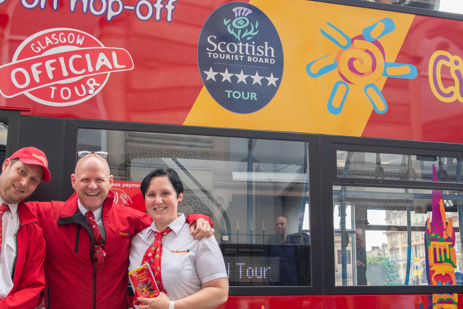 two men and a woman smile infront of City Sightseeing bus
